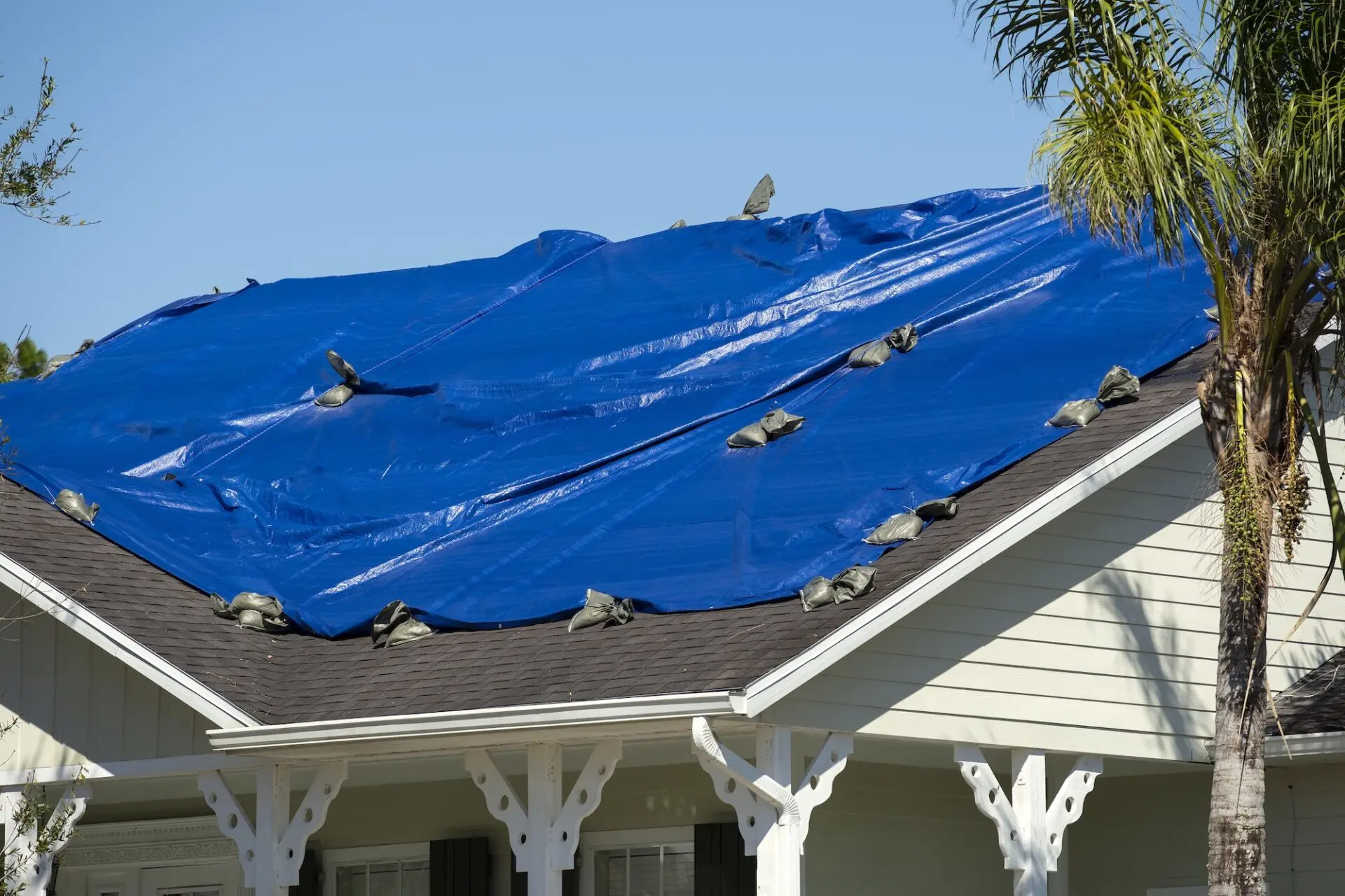 Damaged house roof covered with blue protective tarp against rain water leaking until replacement of asphalt shingles.