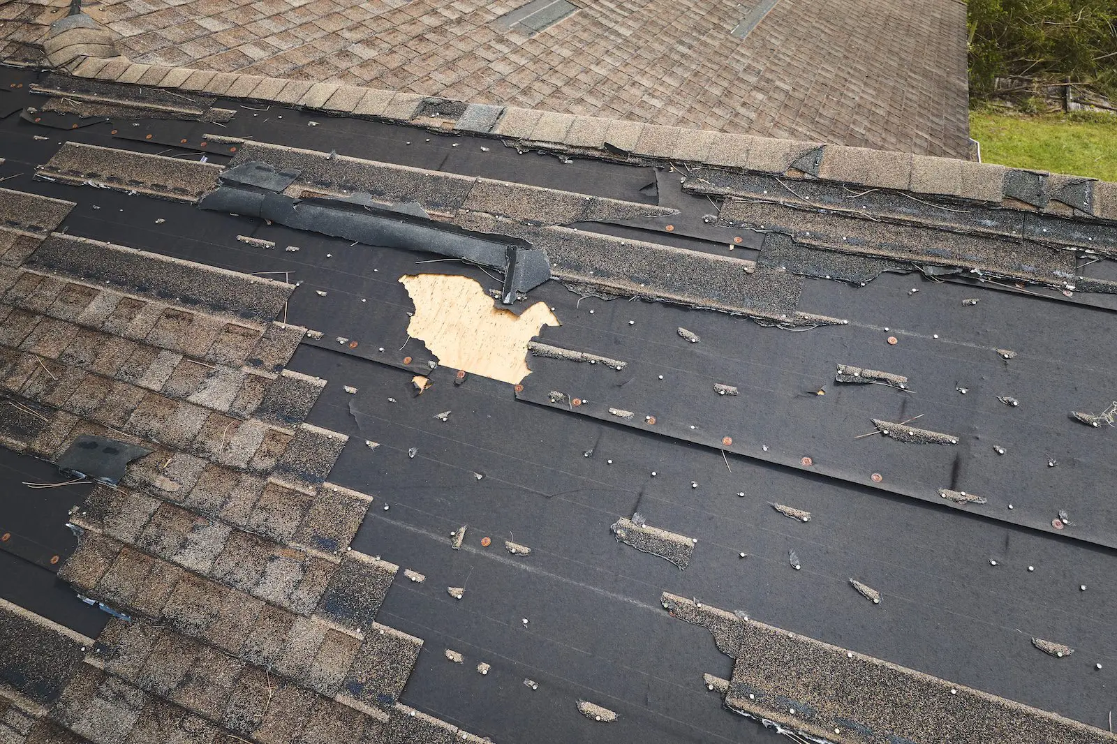 Damaged house roof with missing shingles after major storm.